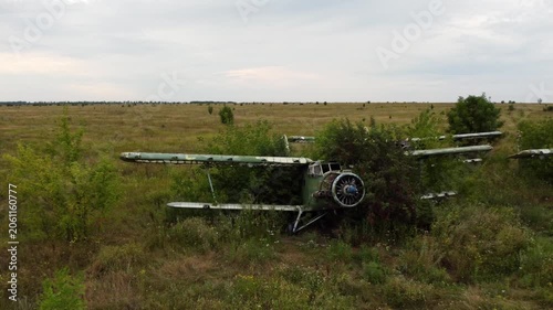 Drone shot of weathered An-2 Antonov biplane abandoned in old airfield, aviation remains in greenery