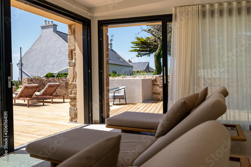 Obraz na plátně Salon luxueux beige et lumineux avec grande baie vitrée offrant une vue panoramique sur une plage paradisiaque, ciel bleu et transats élégants dans une ambiance haut de gamme et relaxante