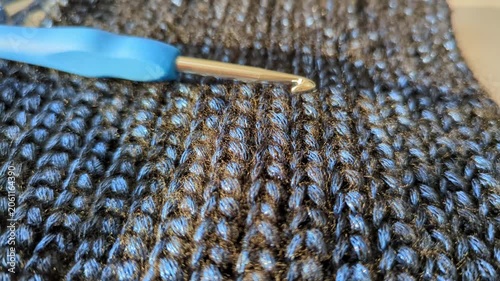 Crochet hook on handmade warm textured, shiny dark blue fabric. Detailed stitches textile craft work
