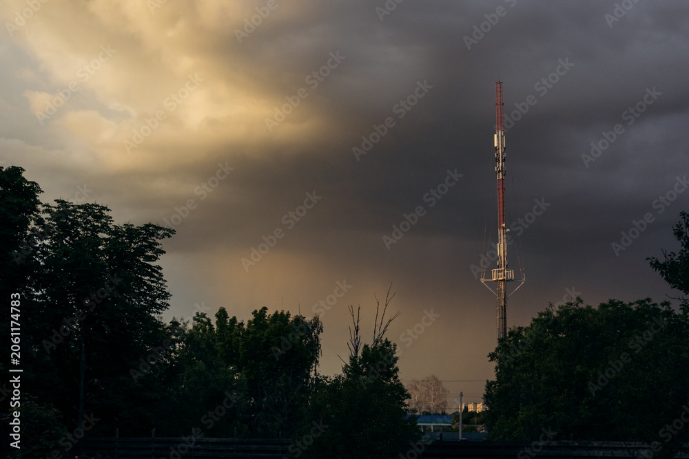 Obraz premium Tall telecommunication tower against dramatic stormy sky at sunset, urban infrastructure concept.