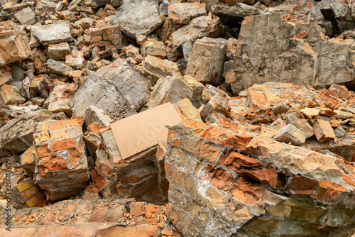 Rubble and bricks scatter across the ground after a building collapse. A piece of cardboard lies among the debris in an urban setting