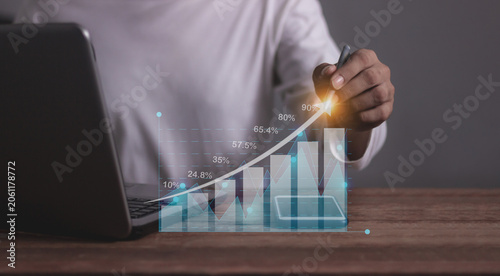 Young man with computer notebook and smartphone hand touching to visualize money growth The phone screen displays graphs and charts showing increasing investment and savings trends, increased account
