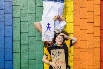 Activists lie outdoors holding equality signs on a rainbow street