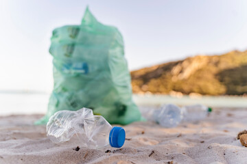 Empty plastic bottles and garbage bin full of collected plastic bottles on the beach