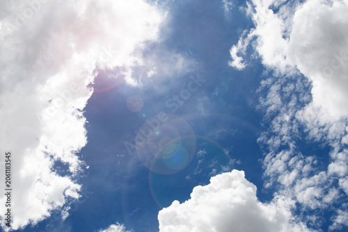 Sunlight shines through the white clouds in the bright blue sky.