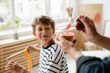 Father offering healthy but sour grapefruit to reluctant son