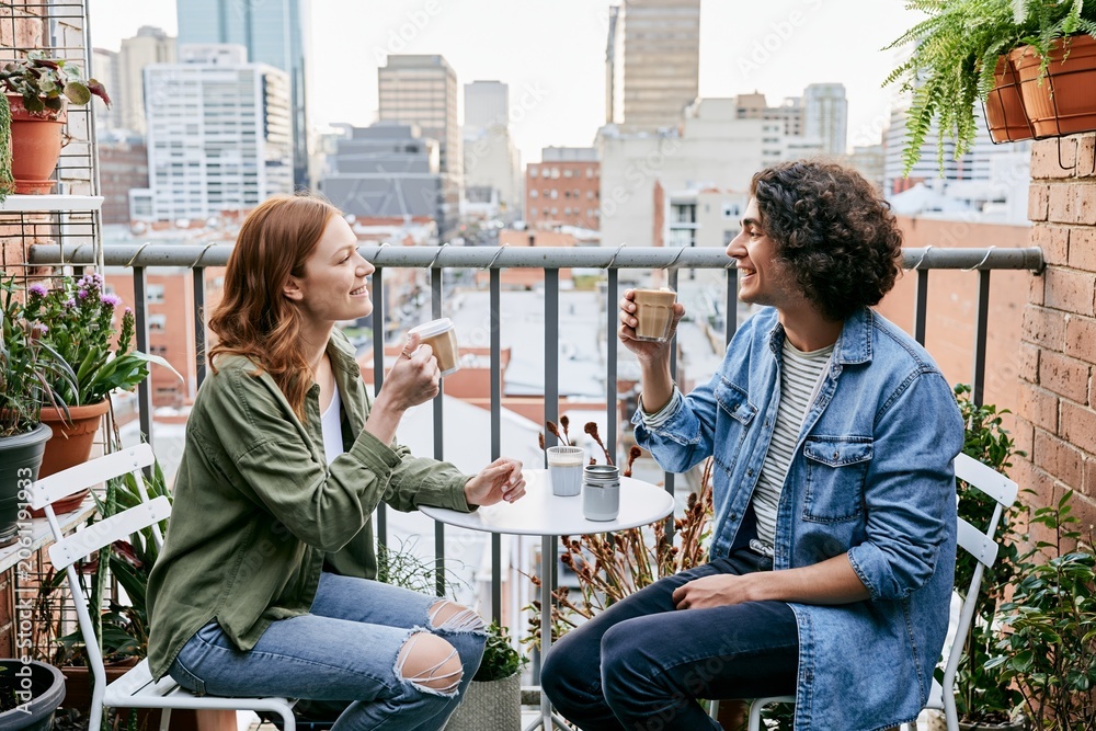 Fototapeta premium Two friends chatting over coffee on rooftop style balcony