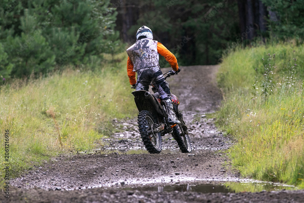 Obraz premium Back enduro racer rides on forest trail through mud and water