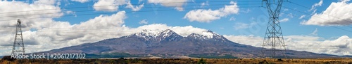 Electrical transmission towers stretch across dry grassland with snow‑covered mountains rising in the distance along Desert Road, New Zealand