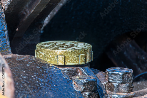 A close-up of a worn yellow metal cap attached to an aged industrial machine surface, showing corrosion, texture, and mechanical detail