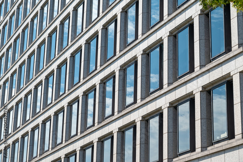Modern office building facade with repetitive windows reflecting the blue sky