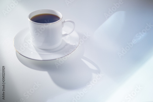 Elegant White Coffee Cup with Gold Rim and Saucer on a White Table in Soft Morning Light with Copy Space. Luxury lifestyle concept. Shallow depth of field.
