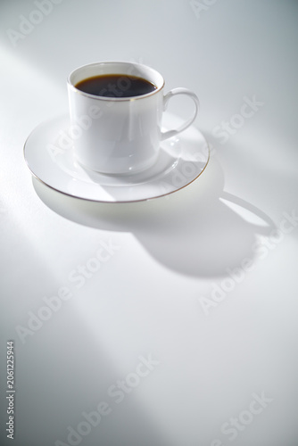 Elegant White Coffee Cup with Gold Rim and Saucer on a White Table in Soft Morning Light with Copy Space. Luxury lifestyle concept. Shallow depth of field.