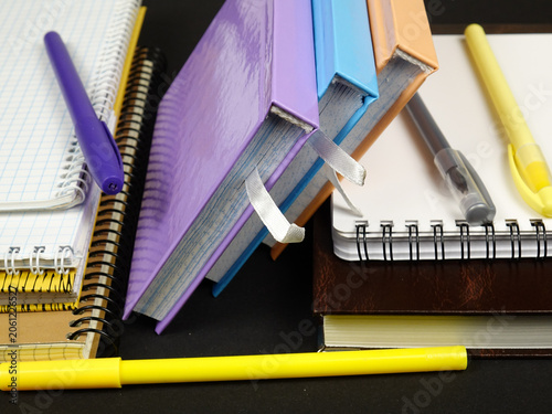 Various types of notepads and ballpoint pens lie on a black table. Sets for notations, studying, note -taking, and diary.
