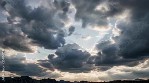 Dramatic cloudy sky with sun rays over mountain landscape at sunset or sunrise