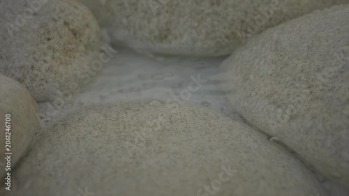 Close-up view of smooth, rounded stones submerged in clear water, showcasing the gentle movement of water and bubbles between the rocks in a natural setting