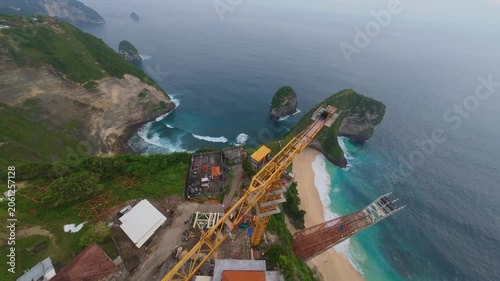 Spectacular FPV drone tracking shot plunging down Kelingking Beach cliffs – Amazing tropical coastal landscape in bright sunny golden light, premium Bali Indonesia tourism advertising background