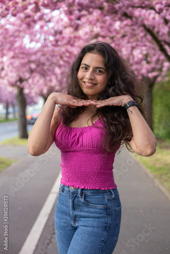 Smiling young woman with hands under chin in cherry blossom spring portrait