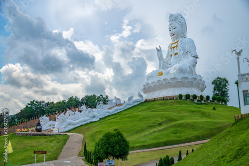 Fotografie Giant white Guan Yin statue sitting on a lotus pedestal on green hill under beautiful blue sky at Wat Huay Pla Kang, Chiang Rai, Thailand
