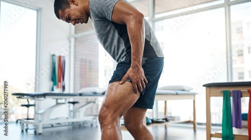 Young man suffering from severe thigh muscle pain in a physical therapy clinic
