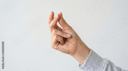A hand against a plain background snapping fingers, wearing a gray long-sleeve shirt and a thin gold bracelet.