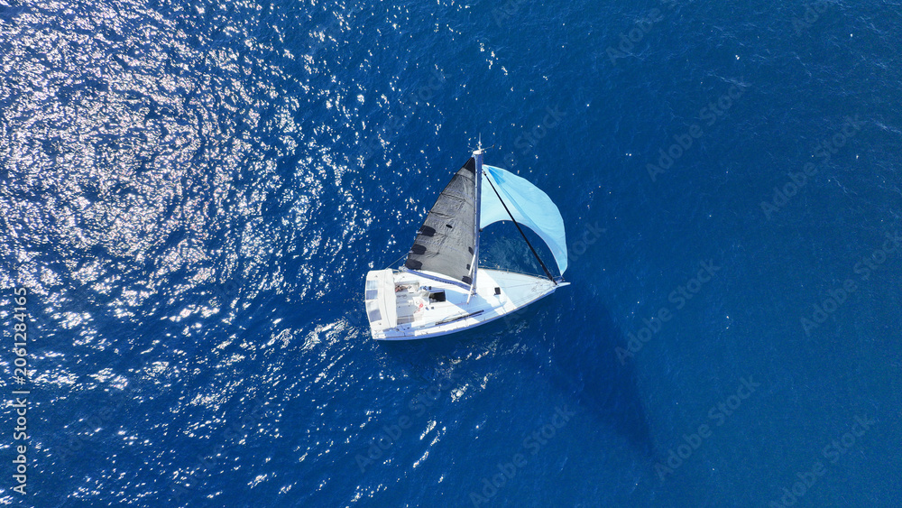 Obraz premium Aerial drone photo of small sail boat with blue sails cruising in deep blue Mediterranean Sea
