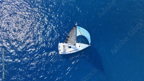 Aerial drone photo of small sail boat with blue sails cruising in deep blue Mediterranean Sea