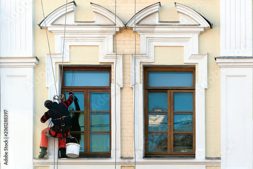 A climber worker meticulously cleaning the windows and facade of a renovated residential building