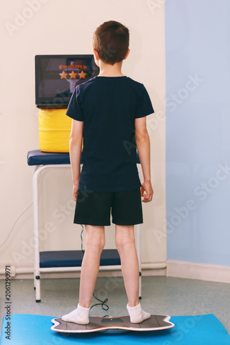 A cute boy is practicing on a balance board for children with cerebral palsy.