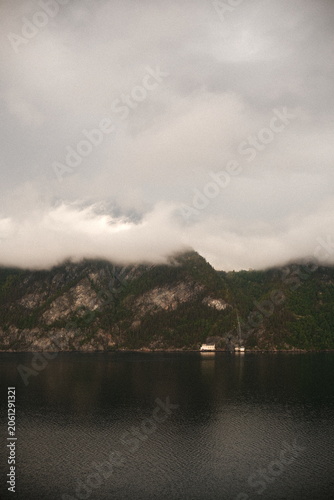 Obraz na płótnie A vast, distant mountain range rendered in rich, brownish earth tones and deep ochre rises in the background, its highest peaks capped by a thick, heavy crown of churning grey clouds