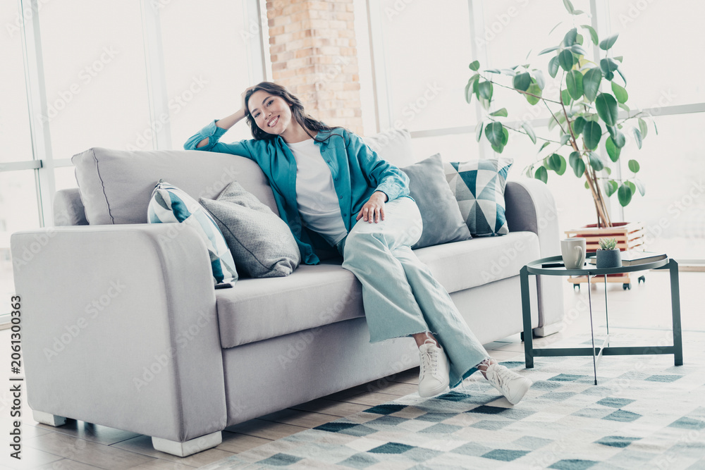 Obraz premium Smiling woman relaxing on a sofa in a bright living room enjoying a comfortable, casual moment at home
