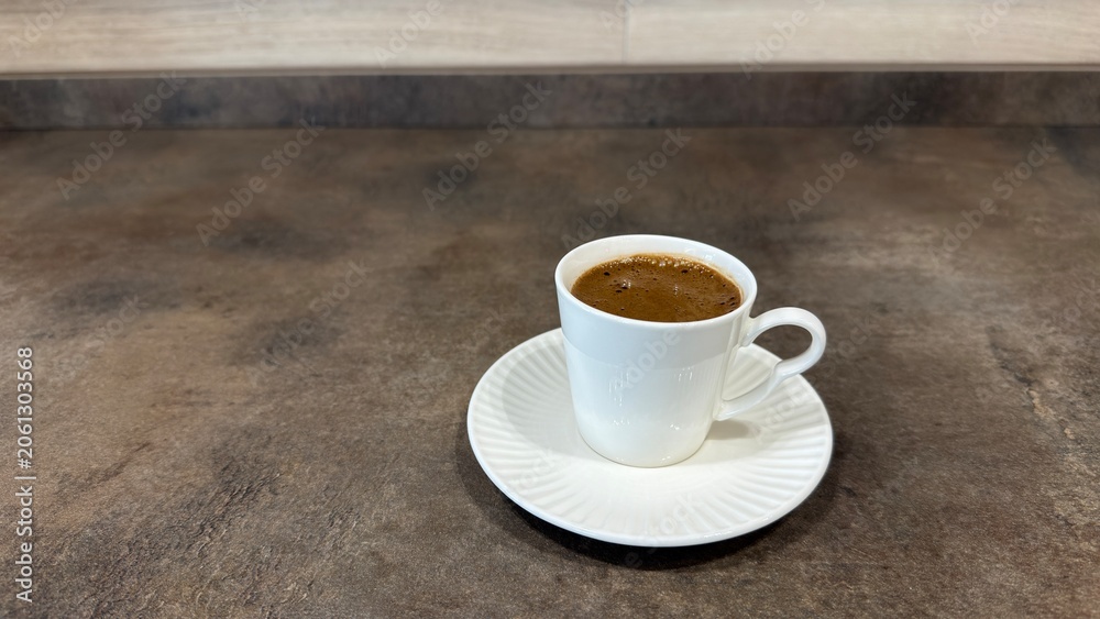 Obraz premium Traditional Turkish coffee in white ceramic cup with saucer on dark textured kitchen countertop, close up high angle view.