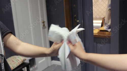 A teenage girl wipes cleaner from a mirror with a paper towel during a household cleaning routine in a home hallway
