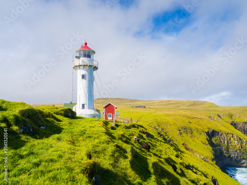 Akraberg Lighthouse on Suduroy Island, Faroe Islands. Sunny summer day landscape with green meadows, cliffs and ocean under a cloudy sky. Postcard background.