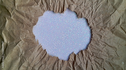 Konstfotografi White holographic glitter texture visible through a torn hole in crumpled brown kraft paper