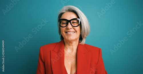 Фотография Smiling mature woman with grey hair and stylish eyeglasses wearing a red blazer,