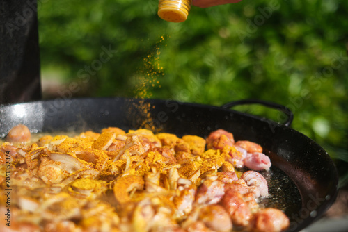 Cooking paella with chicken, vegetables in a frying pan and sprinkled with turmeric, paprika. Selective focus.