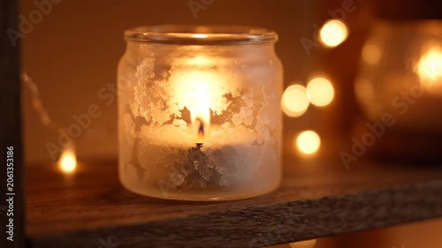 Close-up of a warm glowing candle in a frosted glass jar, creating a cozy and relaxing atmosphere, ideal for hygge, relaxation, or holiday themes