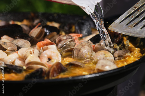 Cooking paella with seafood in a frying pan. Large seafood paella pan being served outdoors. Selective focus.