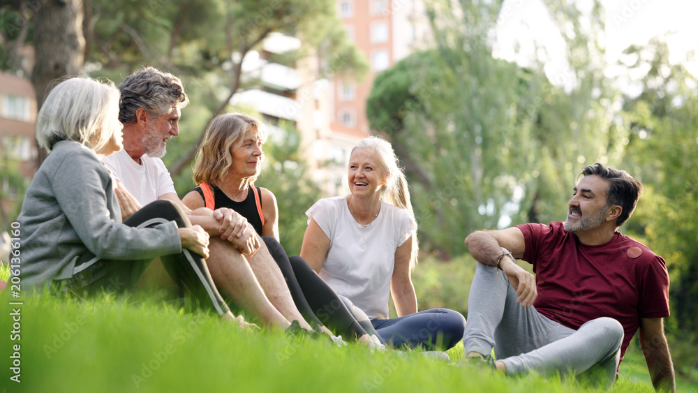 Naklejka premium Group of diverse seniors sitting on grass in a park, talking and laughing after fitness activity, enjoying community and nature