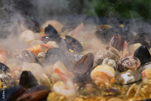 Large seafood paella pan being served outdoors. Hot Vibrant Spanish Paella. Selective focus.