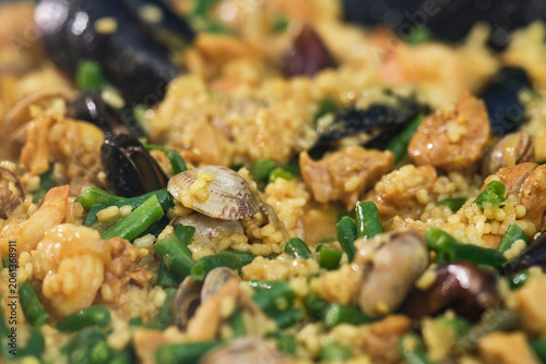Cooking paella with chicken, seafood, and vegetables in a frying pan. Selective focus.
