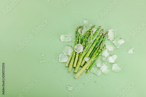 Frozen green asparagus spears covered in hoarfrost with ice cubes on a green background