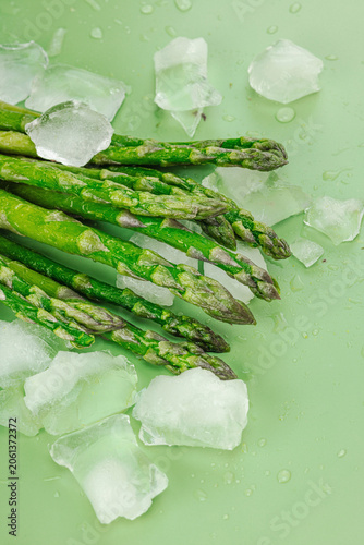 Frozen green asparagus spears covered in hoarfrost with ice cubes on a green background
