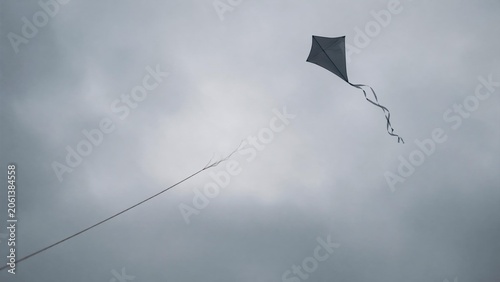 Broken kite string, kite drifting away in gray overcast sky, minimalist composition.