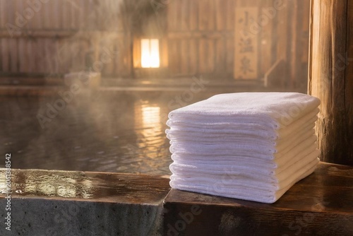 Stack of folded towels beside a steamy bath, warm ambient light.