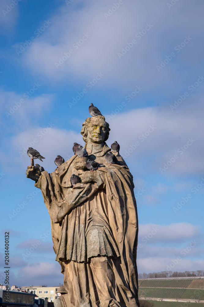 Fototapeta premium Stone statue covered with pigeons against a blue sky