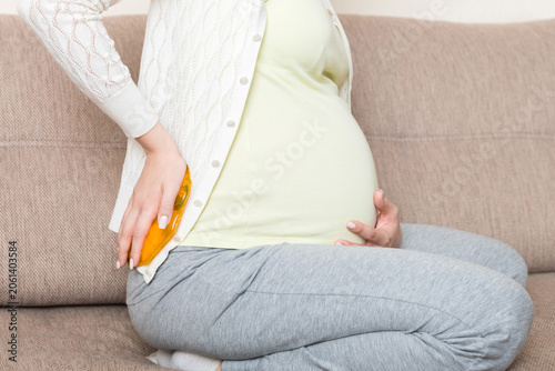 Φωτογραφία Pregnant woman suffer from back pain holds a hot bottle or warmer against her back