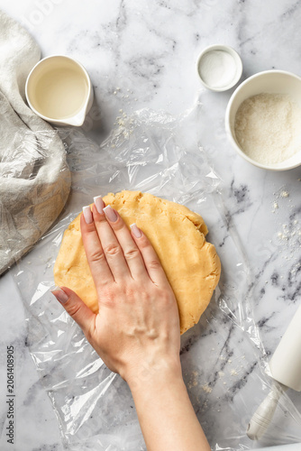 Process of making a base for shortbread pie, tart or quiche. Female hands knead the dough on cling film for subsequent cooling. Home baking culinary concept, recipe. Flat lay