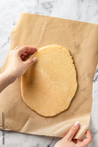 Process of making a base for shortbread pie, tart or quiche. Woman's hands put the dough on a parchment for rolling. Home baking culinary concept, recipe. Flat lay